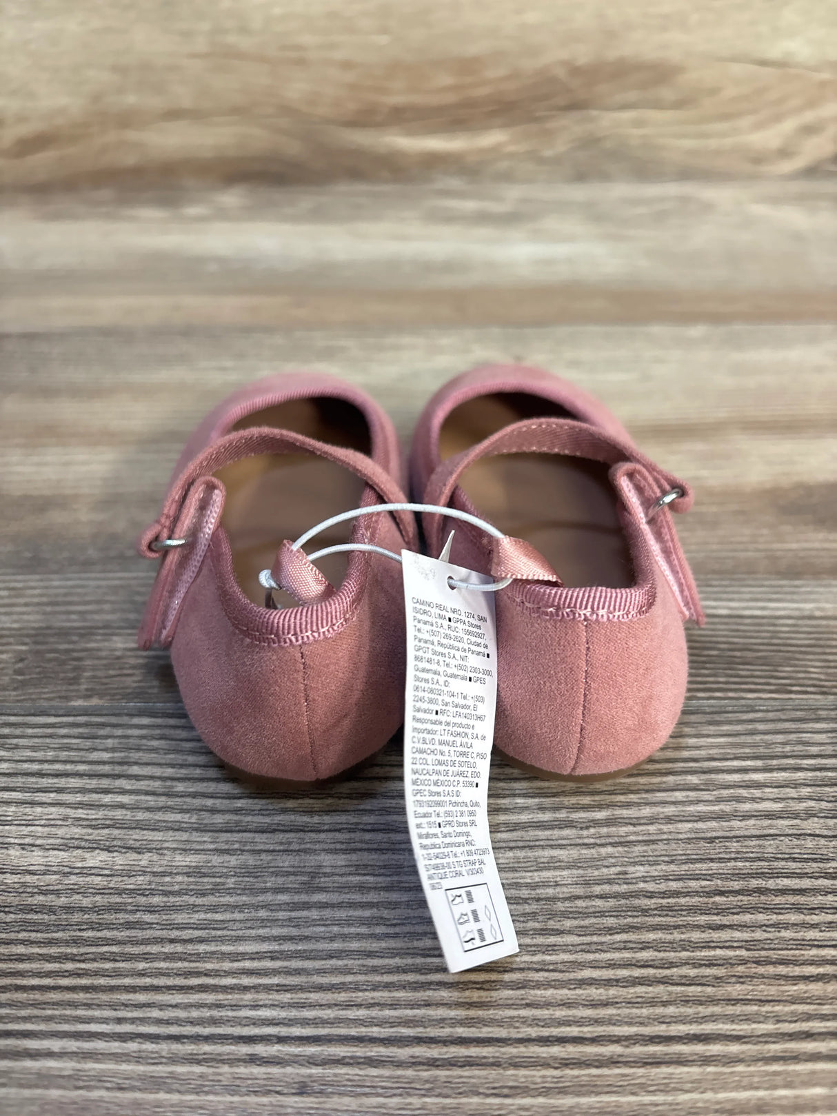 Pink baby girl suede shoes with ankle straps and tag on wooden surface