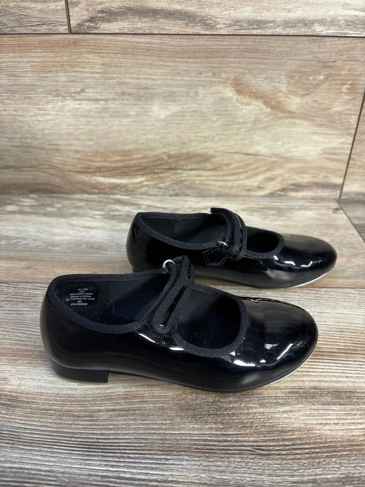Pair of black patent leather children's tap dance shoes on a wooden surface.