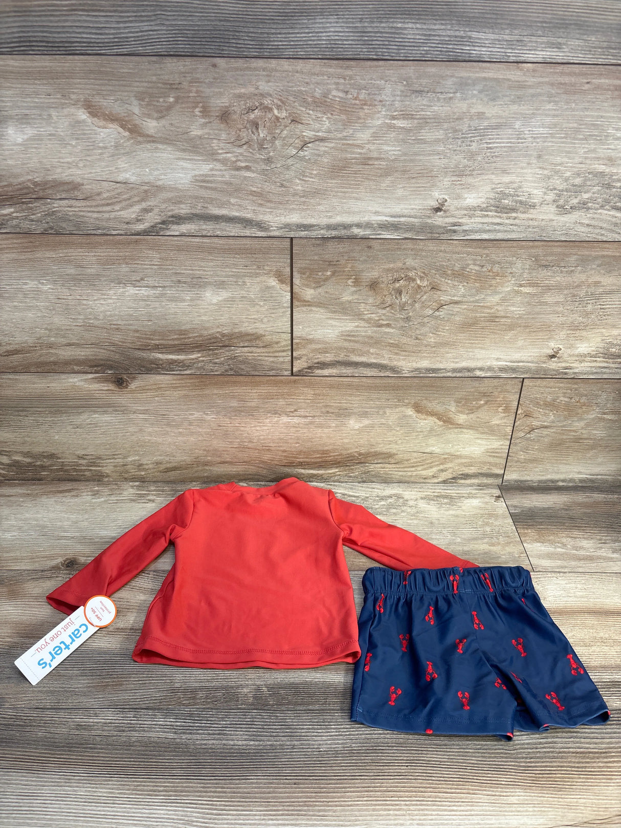 Red long sleeve toddler shirt with navy blue lobster print shorts laid on wood background