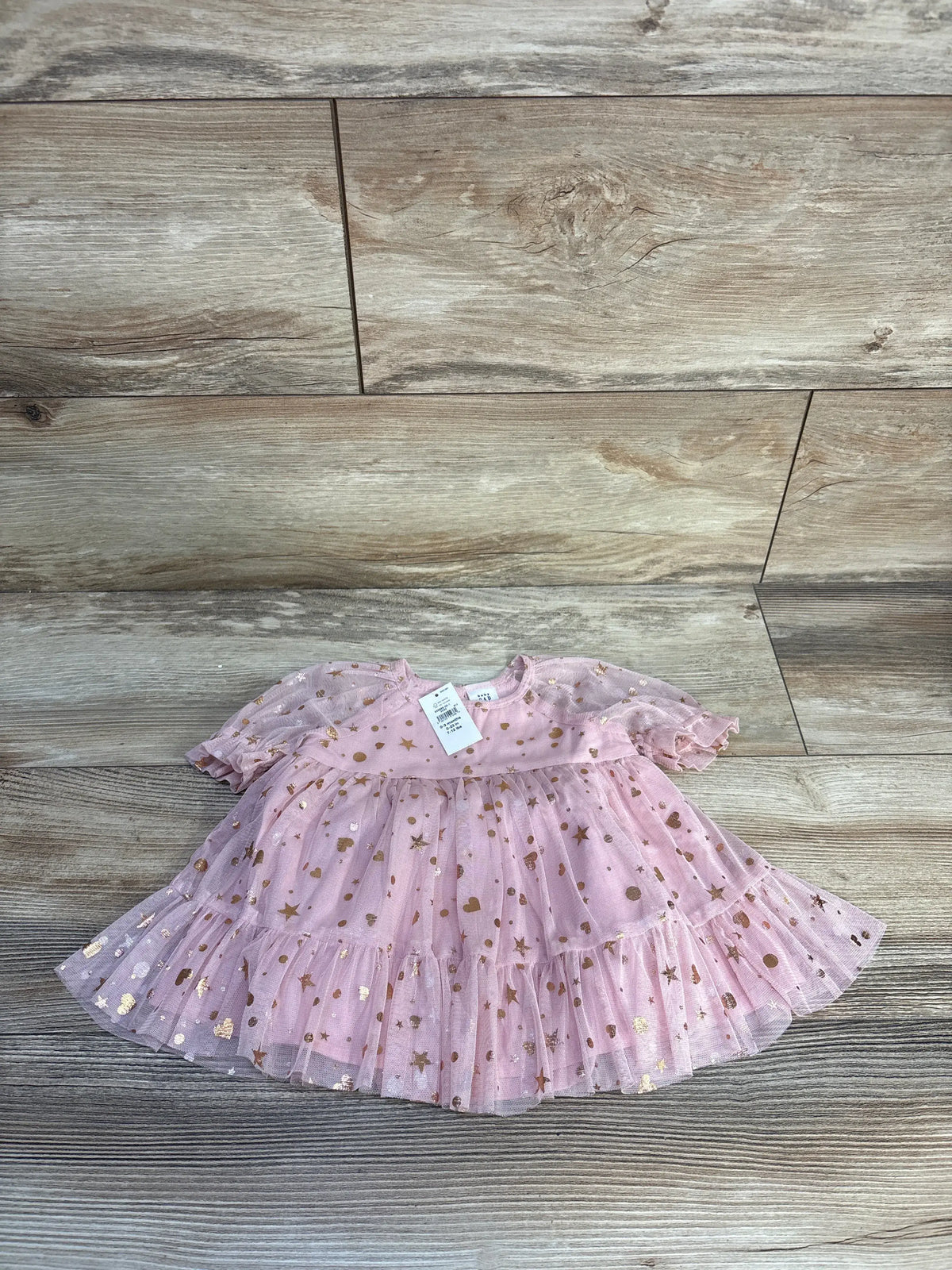 Front view of Baby Gap pink metallic tulle dress with star and heart details, tiered ruffled skirt, and puff sleeves on wood flooring