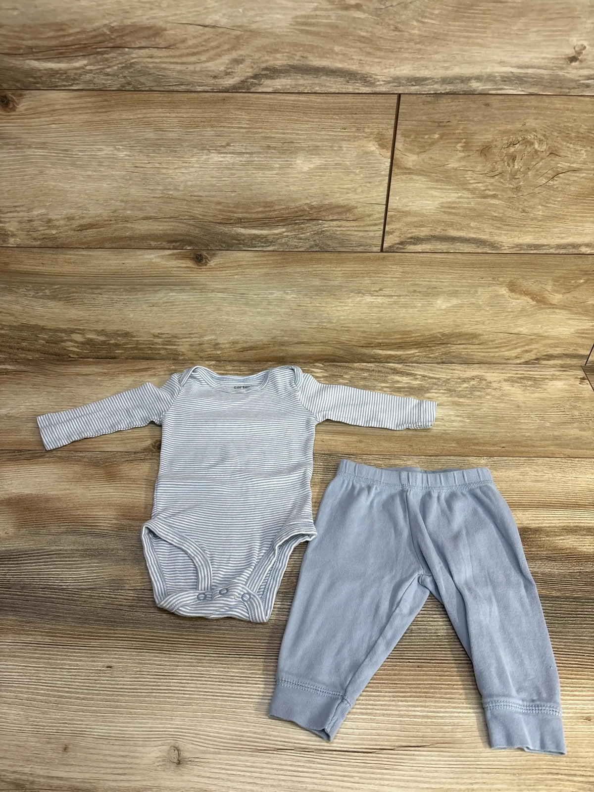Flat lay of blue striped long-sleeve baby bodysuit with crotch snaps and matching light-blue pants on wood floor