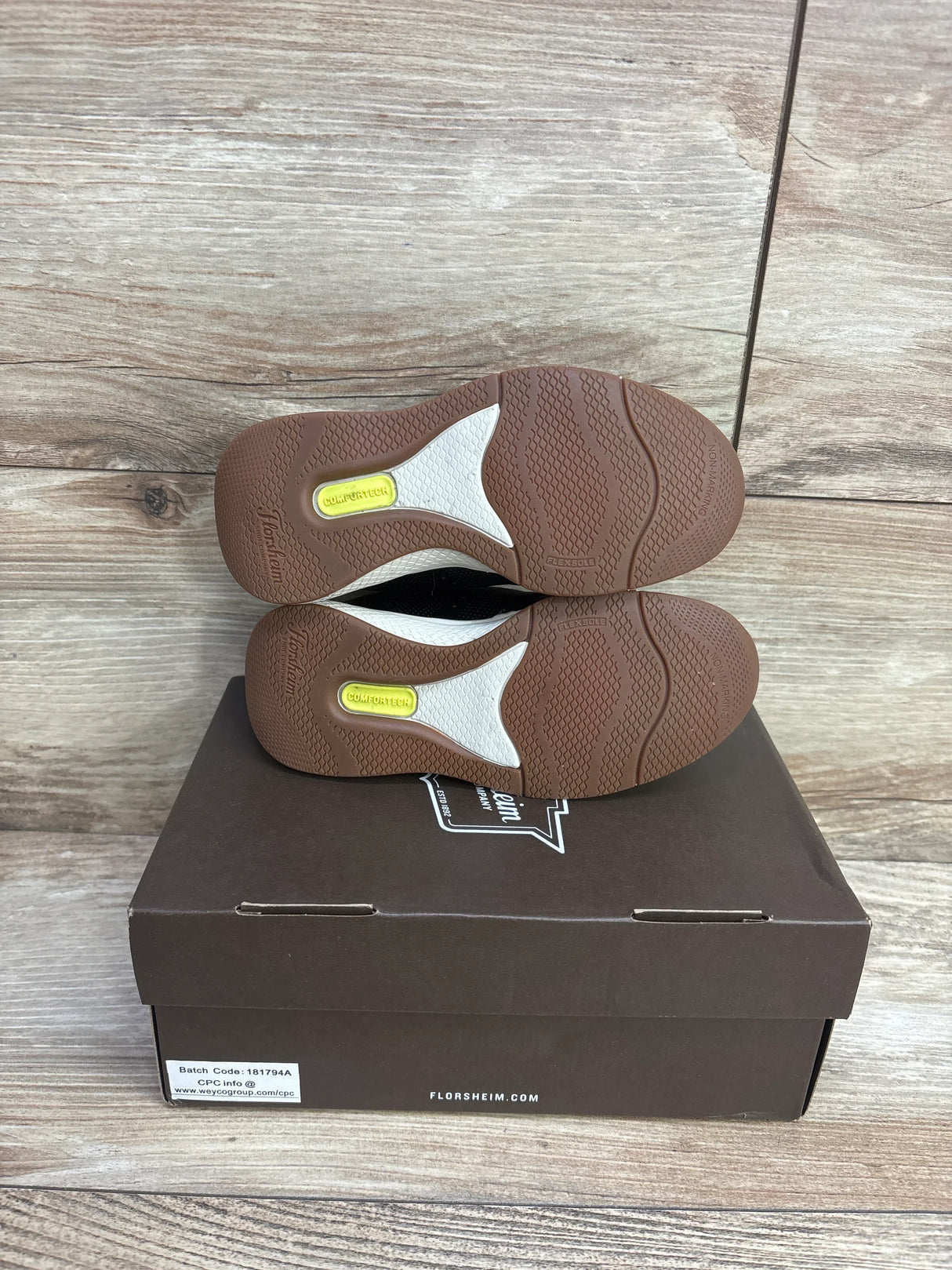 Pair of brown sole kids shoes with Comfortech label on a Florsheim shoe box, wood background