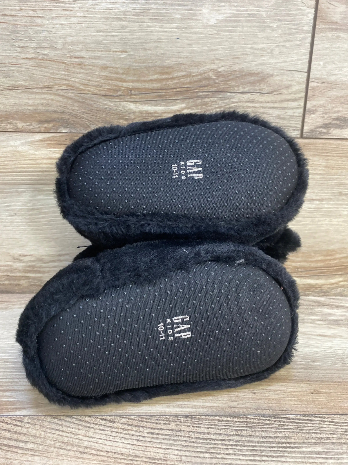 Black faux fur baby slippers with non-slip soles on wood floor, size 10-11