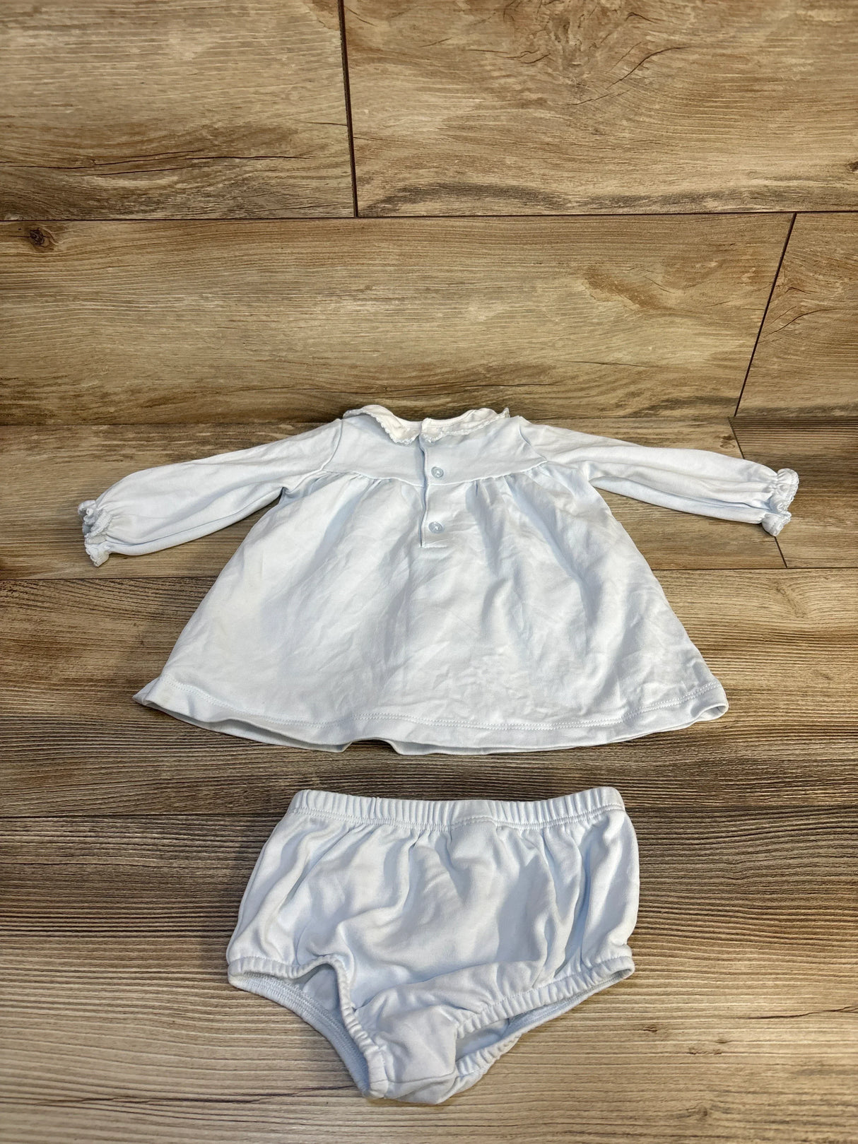 White baby girl long sleeve top with ruffled collar and matching bloomers on wood floor