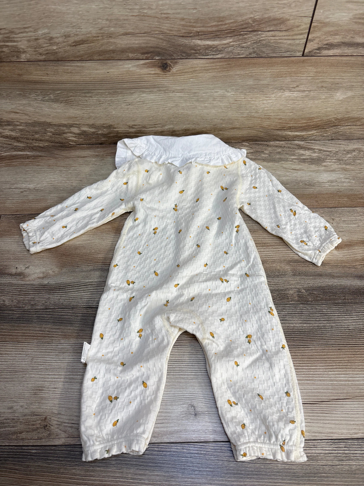 White baby romper with yellow polka dot pattern and ruffle collar on wood floor