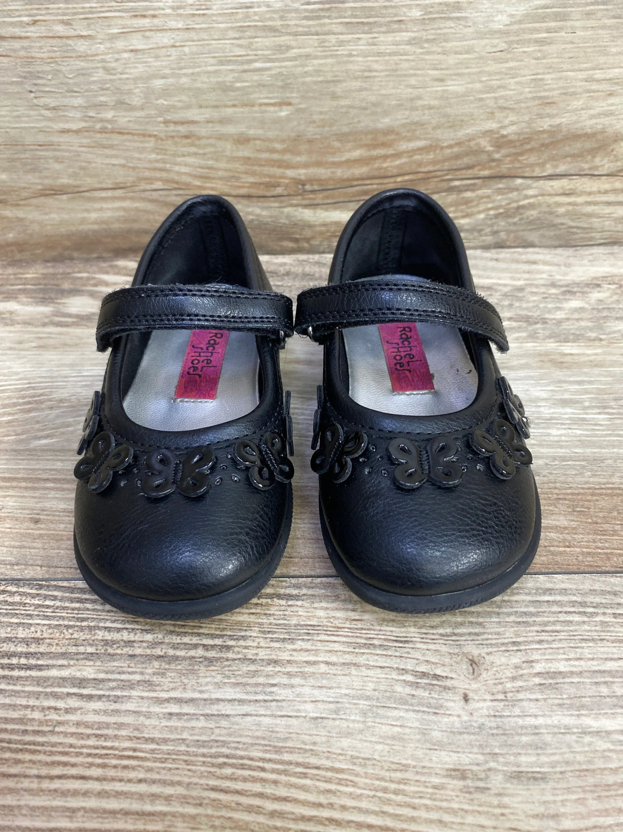 Black toddler Mary Jane shoes with butterfly appliqué on wooden floor