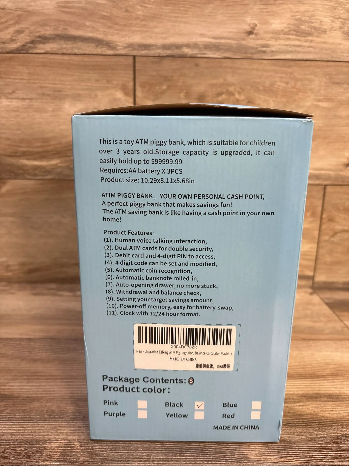 Rear view of Fishboy Talking ATM Piggy Bank box showcasing printed product features, barcode, and checked color boxes on a wooden floor