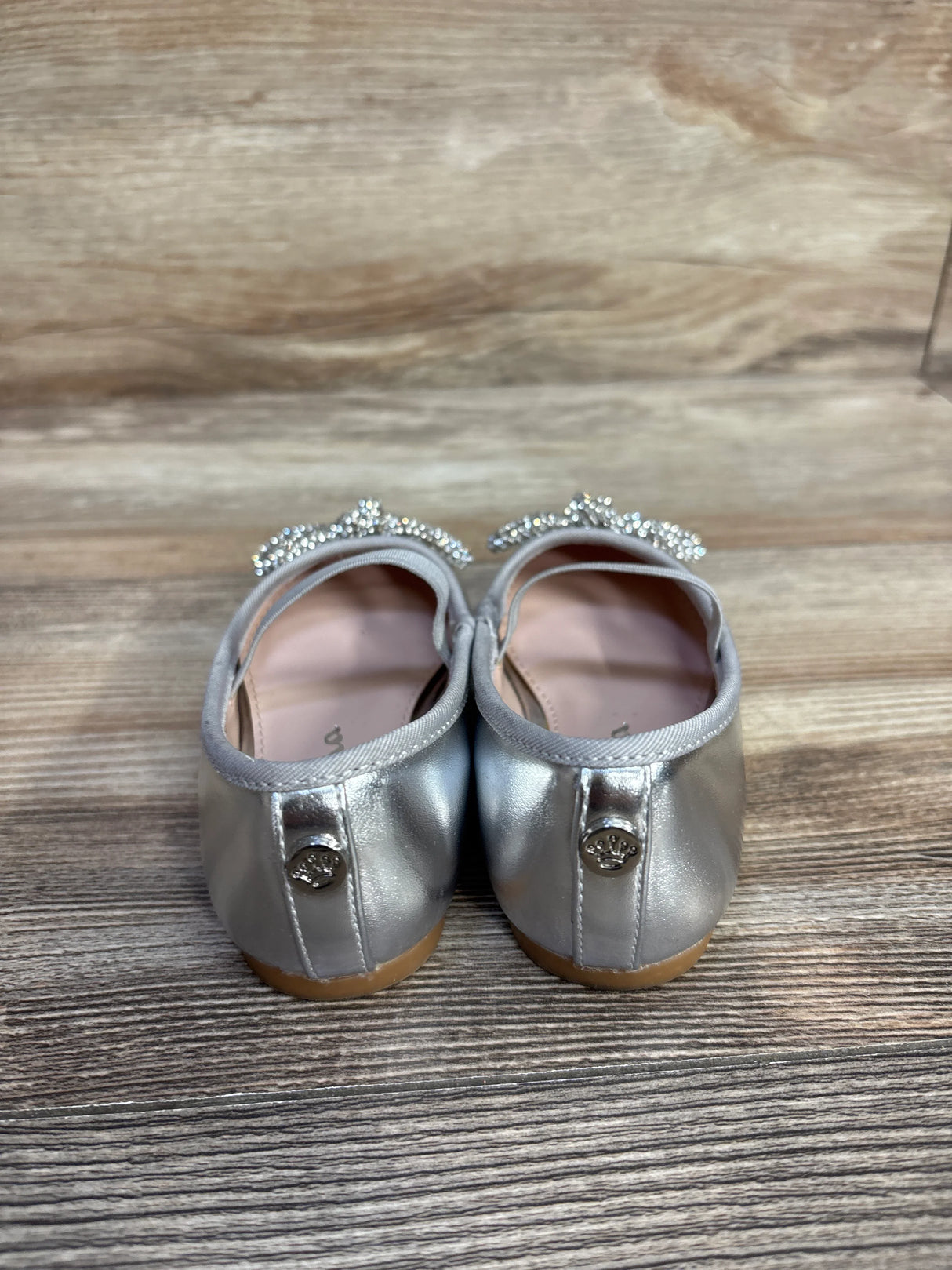 Silver toddler girl dress shoes with rhinestone tiara detail, wood floor background
