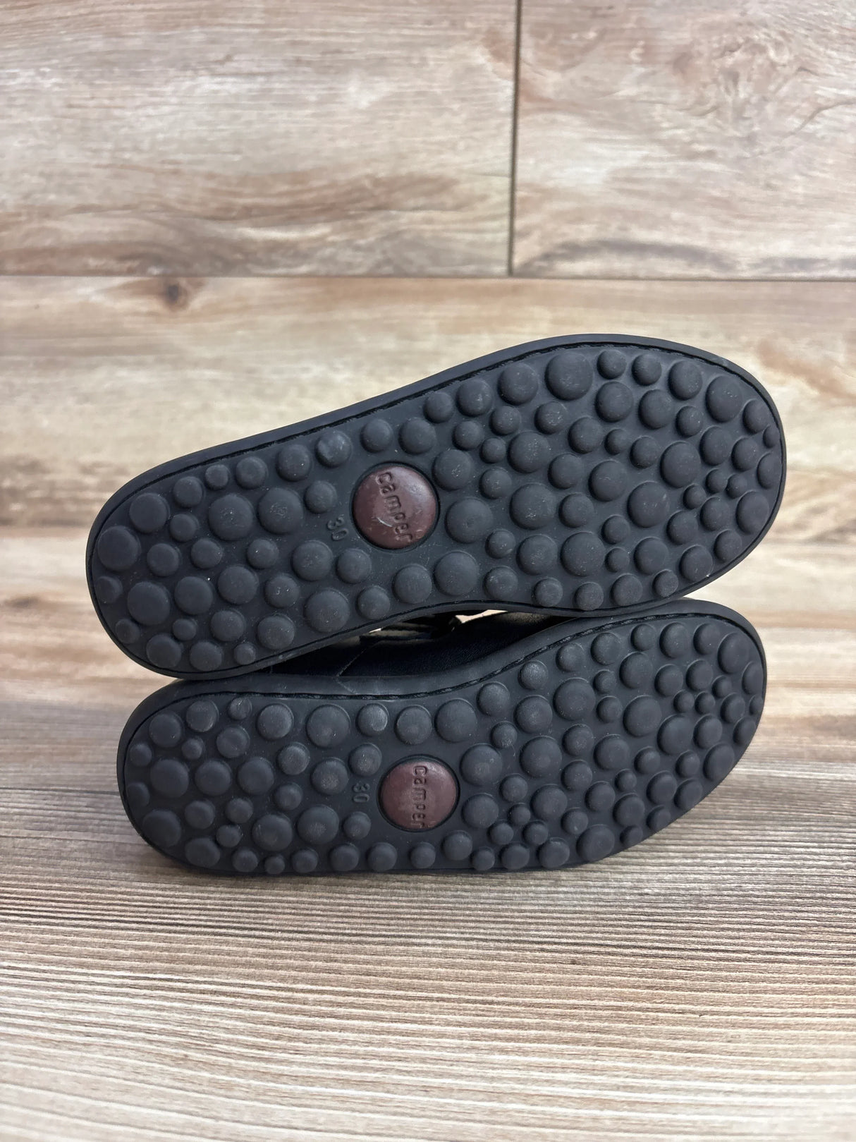 Kid's black shoes with textured Camper rubber soles on wood floor