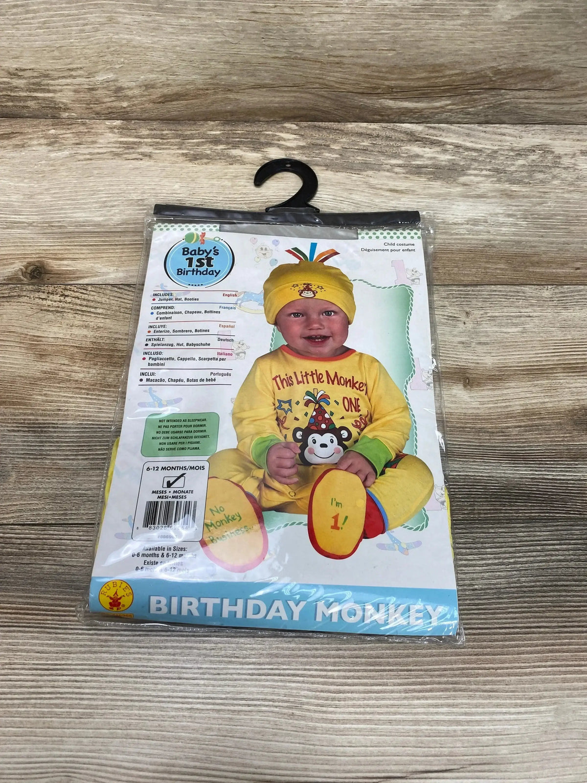 Front view of Rubie’s Birthday Monkey costume package showcasing a yellow outfit with hat and booties on a wood surface