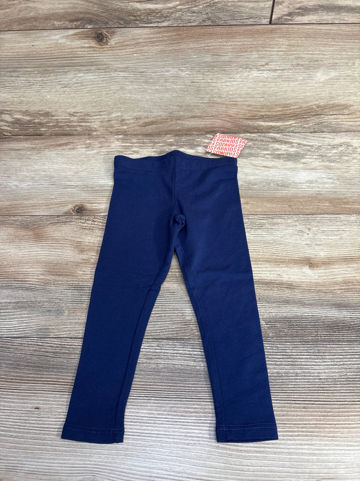 Navy blue children's leggings with fabric tag on wooden floor background