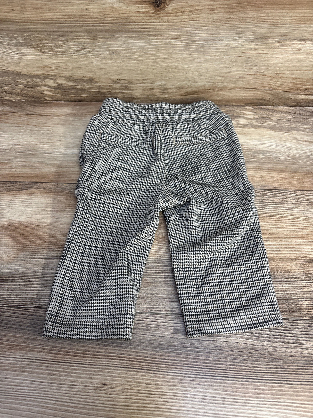Flat lay back view of size 12-month toddler houndstooth tapered knit pants showcasing elastic waistband and faux back pockets on wood floor