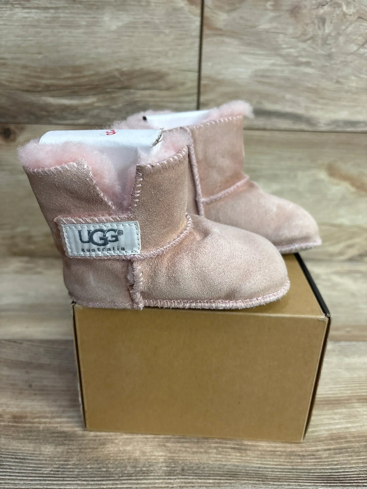 Pair of pink UGG Australia baby booties with soft lining displayed on a brown cardboard box