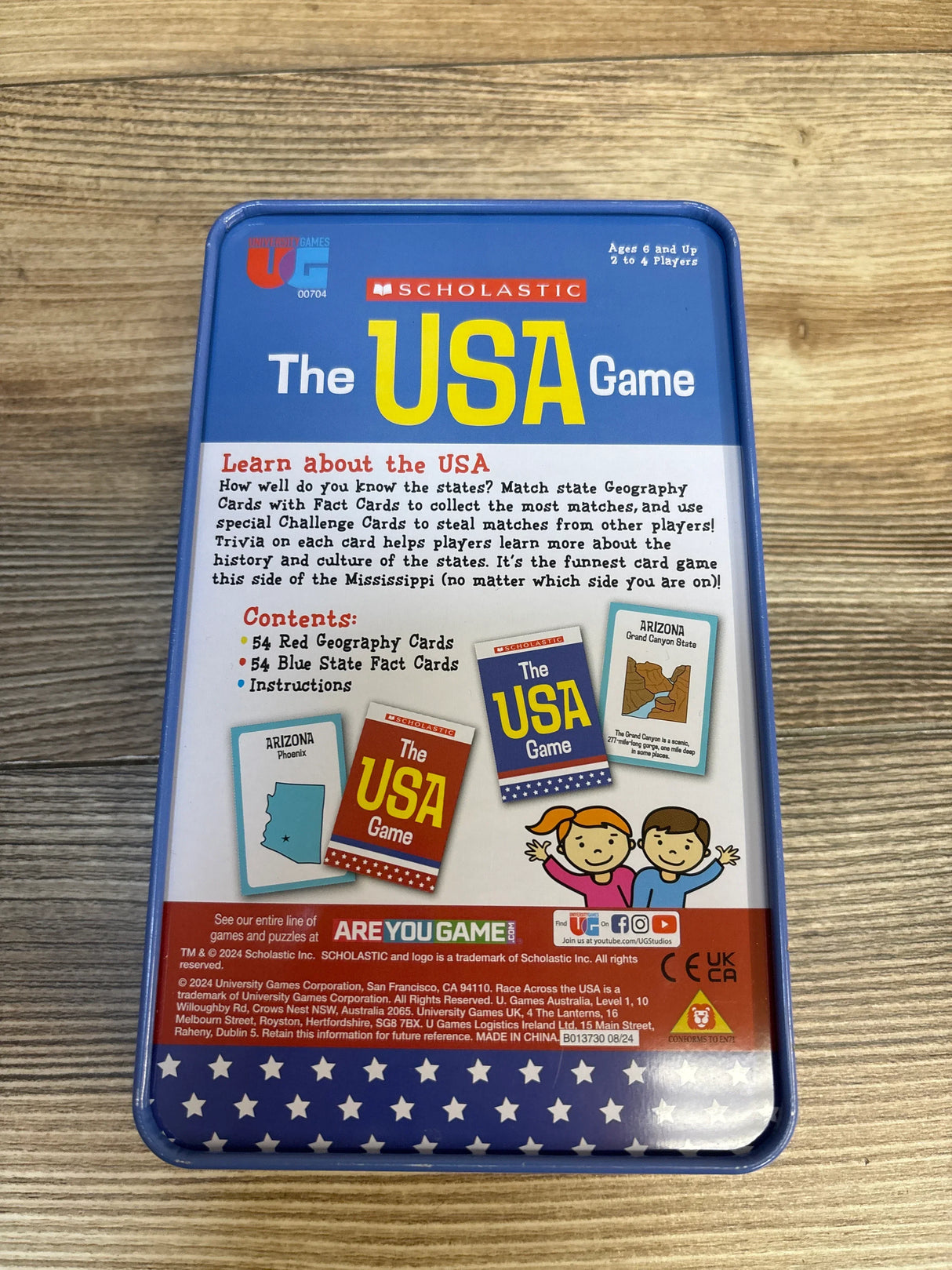 Back view of Scholastic The USA Game card game tin showing contents description and Arizona sample cards on wood plank floor
