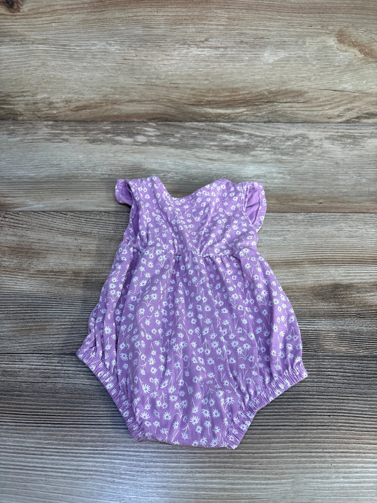 Front view of Okie Dokie bubble romper showcasing purple floral print and gathered bubble legs on a wood-grain background
