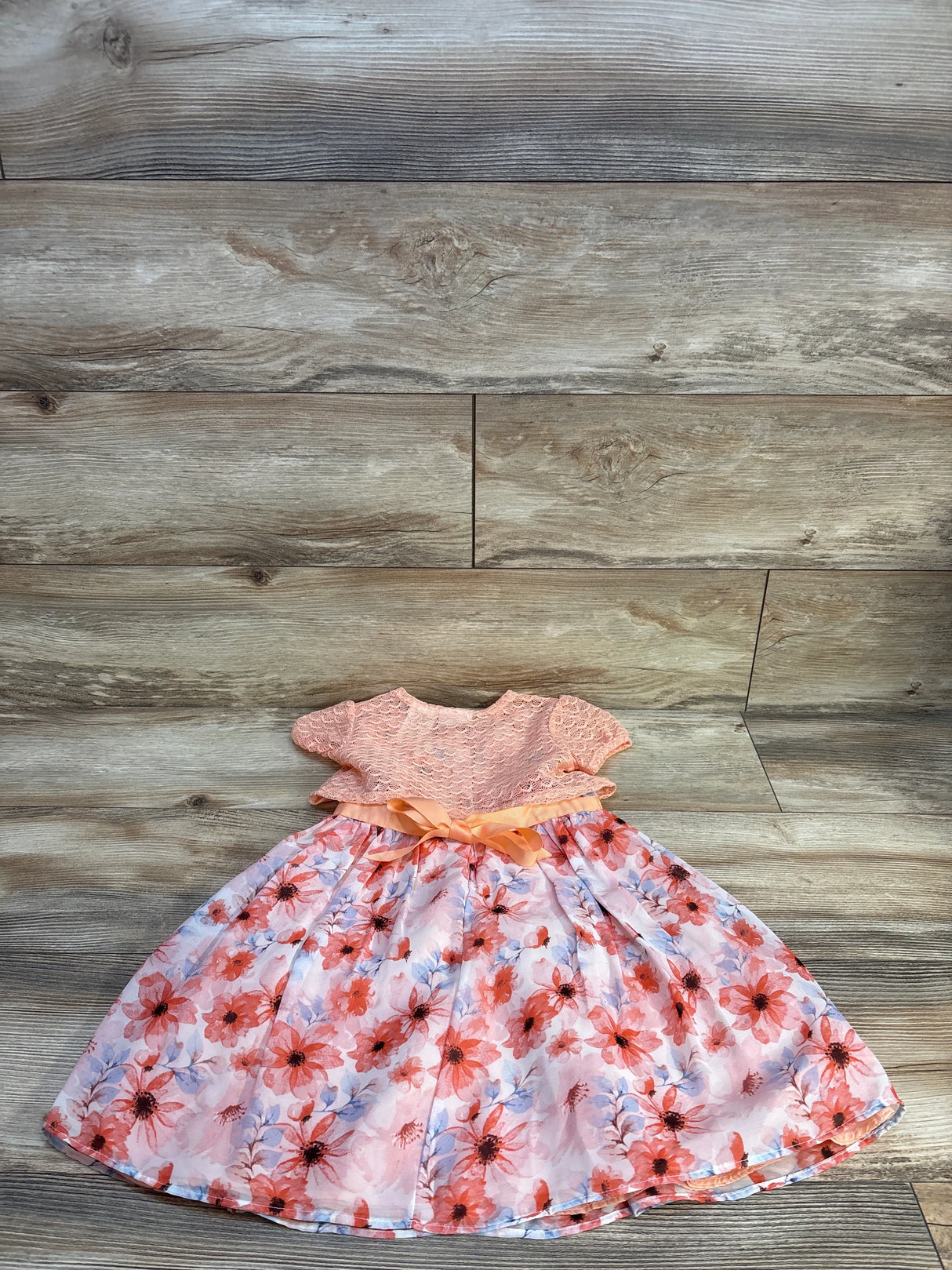 Peach and pink floral baby girl dress with lace bodice and satin ribbon on wood background
