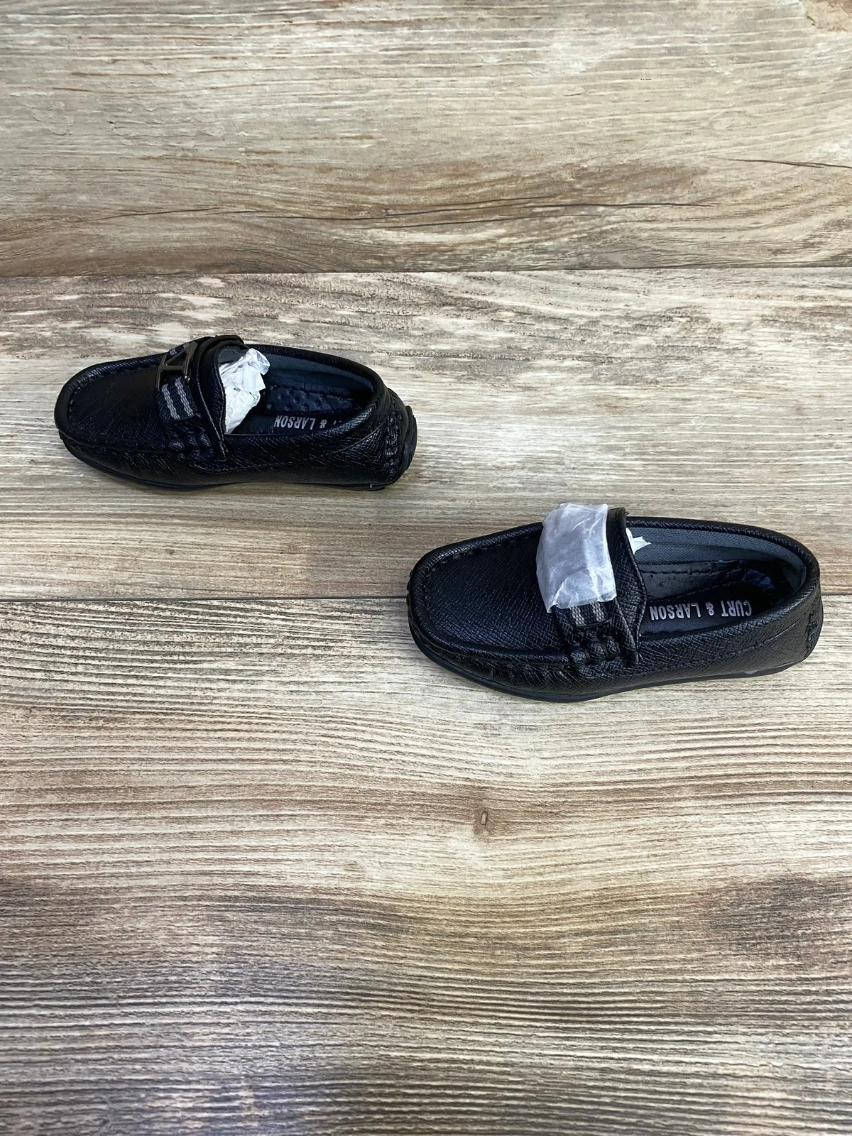 Top view of toddler black Curt & Larson loafers size 5C showing leather texture and braided strap on wood background