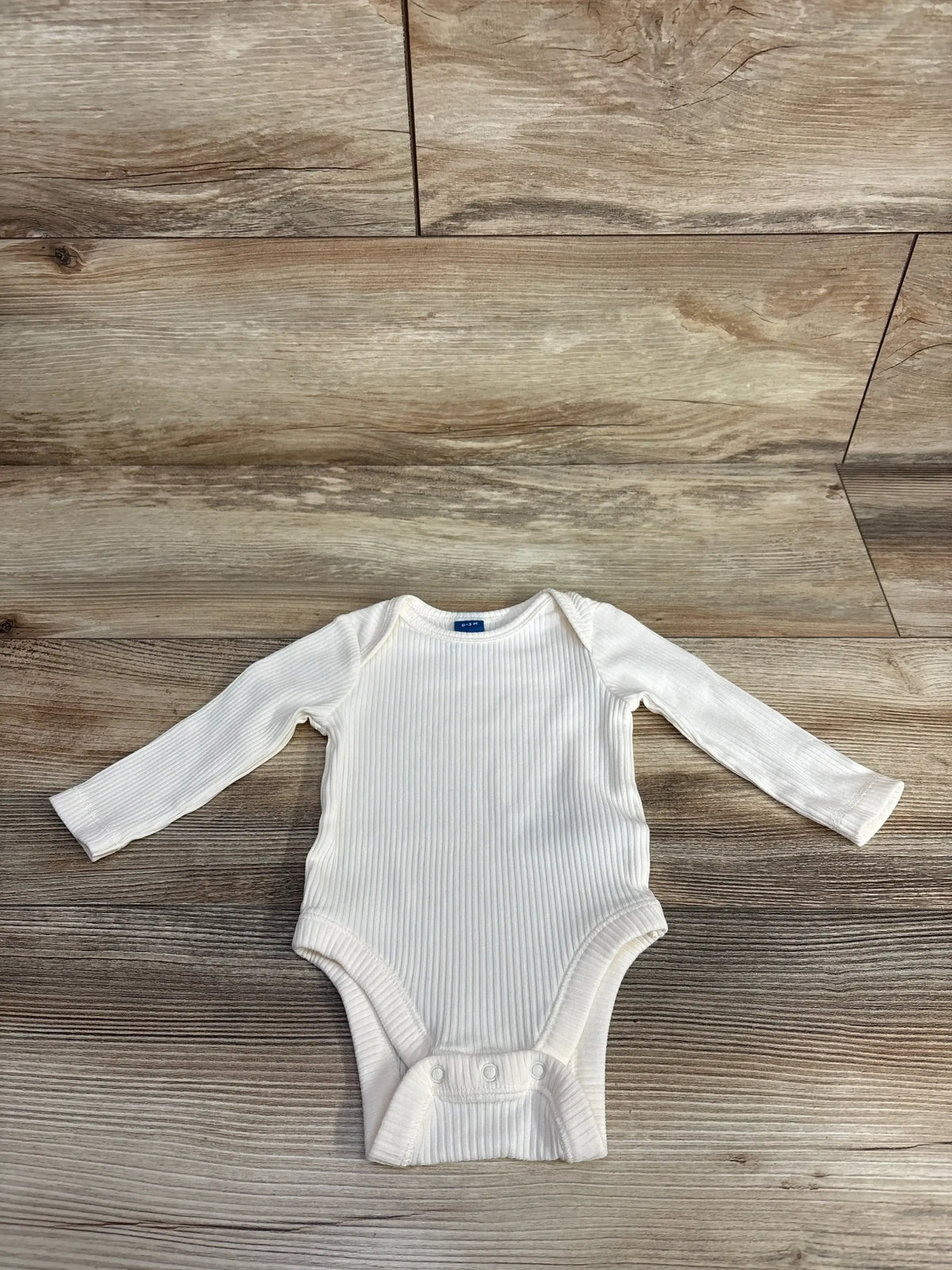 White ribbed long sleeve baby onesie on wooden background, gently used kids clothing