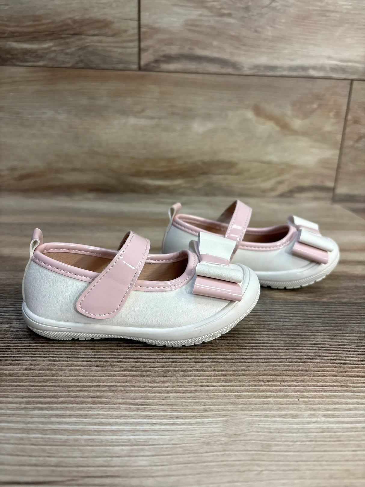 Pink and white toddler Mary Jane shoes with bows on wooden floor
