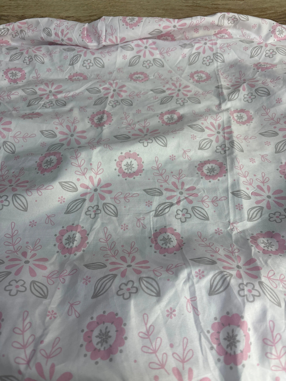 Top-down view of Peanutshell fitted crib sheet showcasing pink and gray floral pattern on white background with a folded edge and wood floor visible