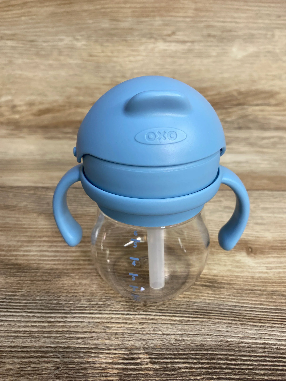 OXO blue handled sippy cup with straw on wood surface