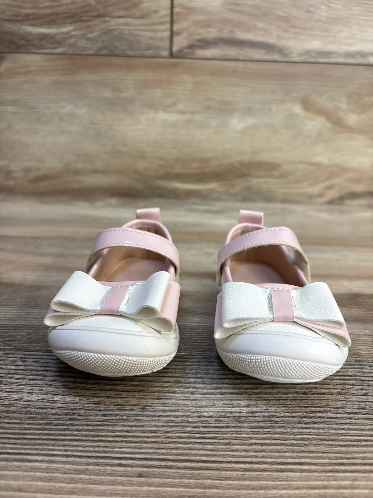 Front view of Mary Jane bow flats in white and pale pink showing white bows and hook-and-loop straps on wooden floor