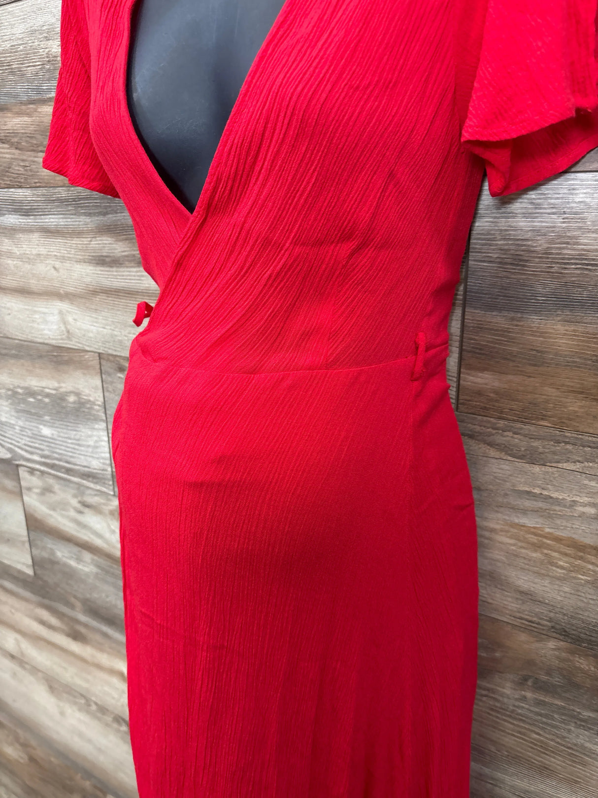 Front close-up of Lulus Much Obliged red wrap maxi dress showcasing surplice bodice and waist tie on wood background