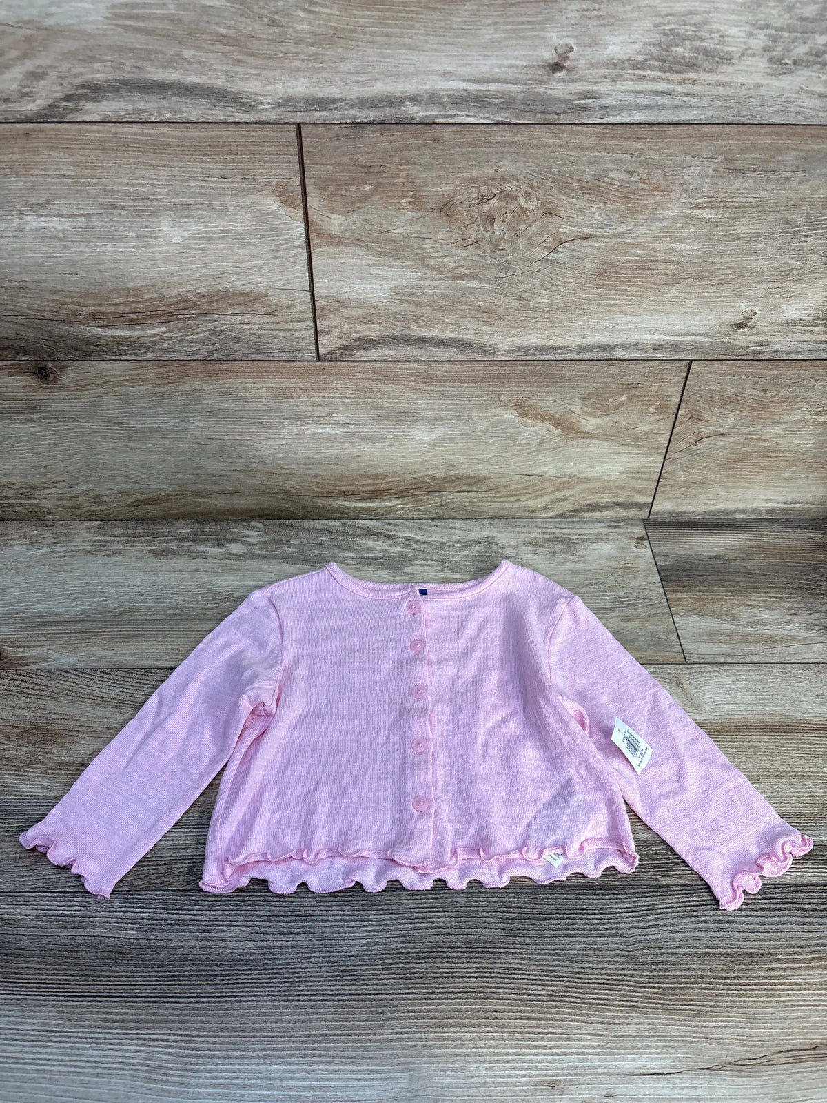 Front view of a pink Old Navy button-up cardigan for ages 18 to 24 months showcasing ruffled trim and long sleeves on a wood-grain background