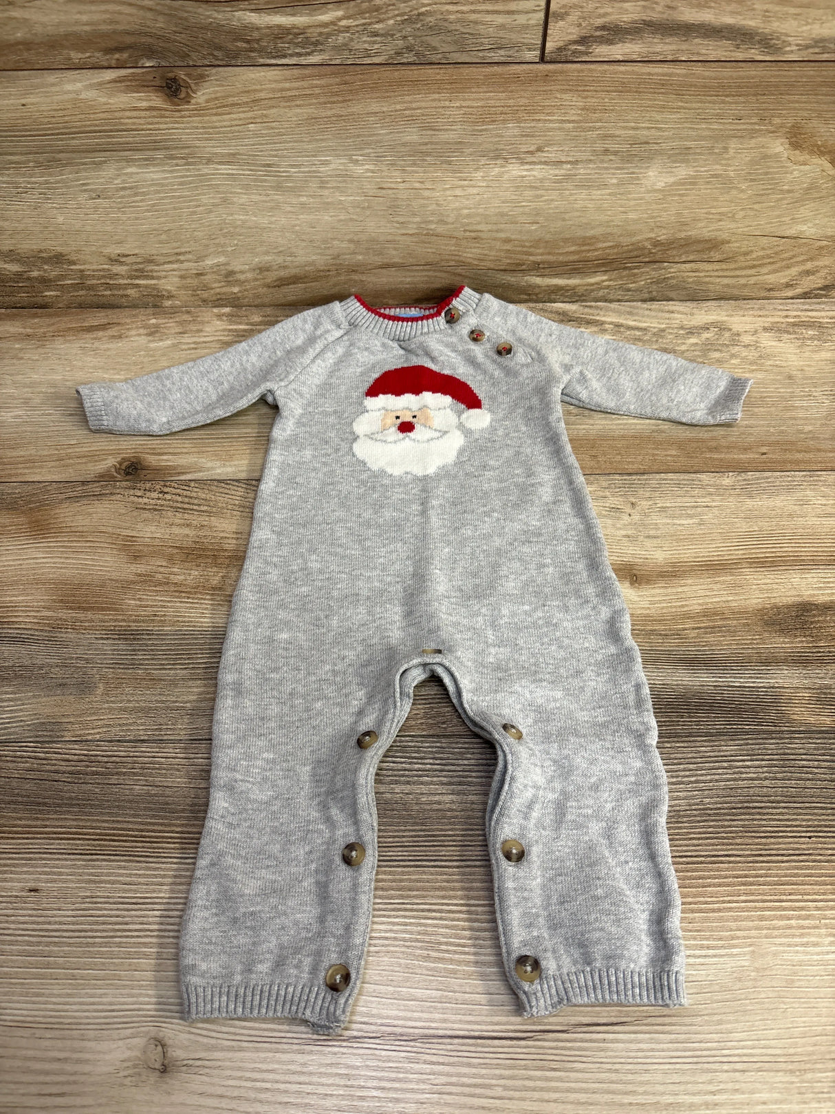 Gray baby onesie with Santa face print, long sleeves, and snap buttons on wood floor