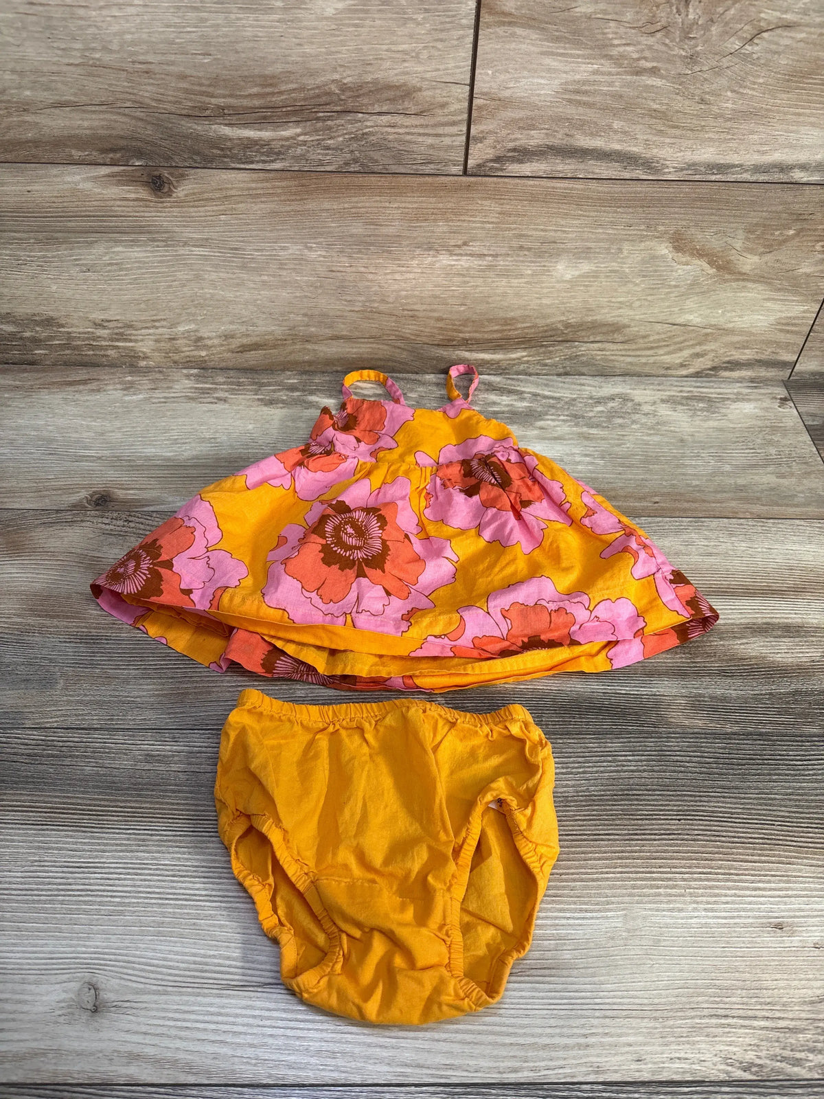 Front view of Baby Gap floral dress and bloomers set showcasing orange floral print on a wood look background