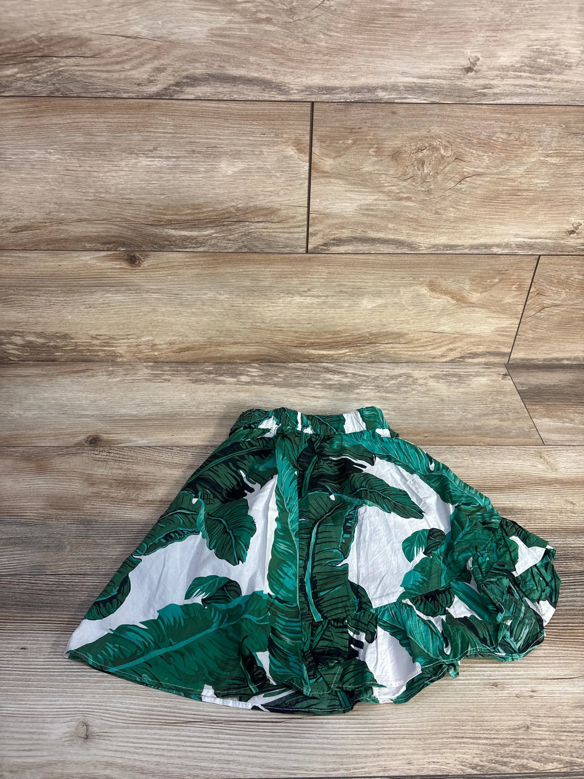 Top view of green tropical skirt in size 2T showcasing its vibrant tropical leaf print with a wood-look floor background