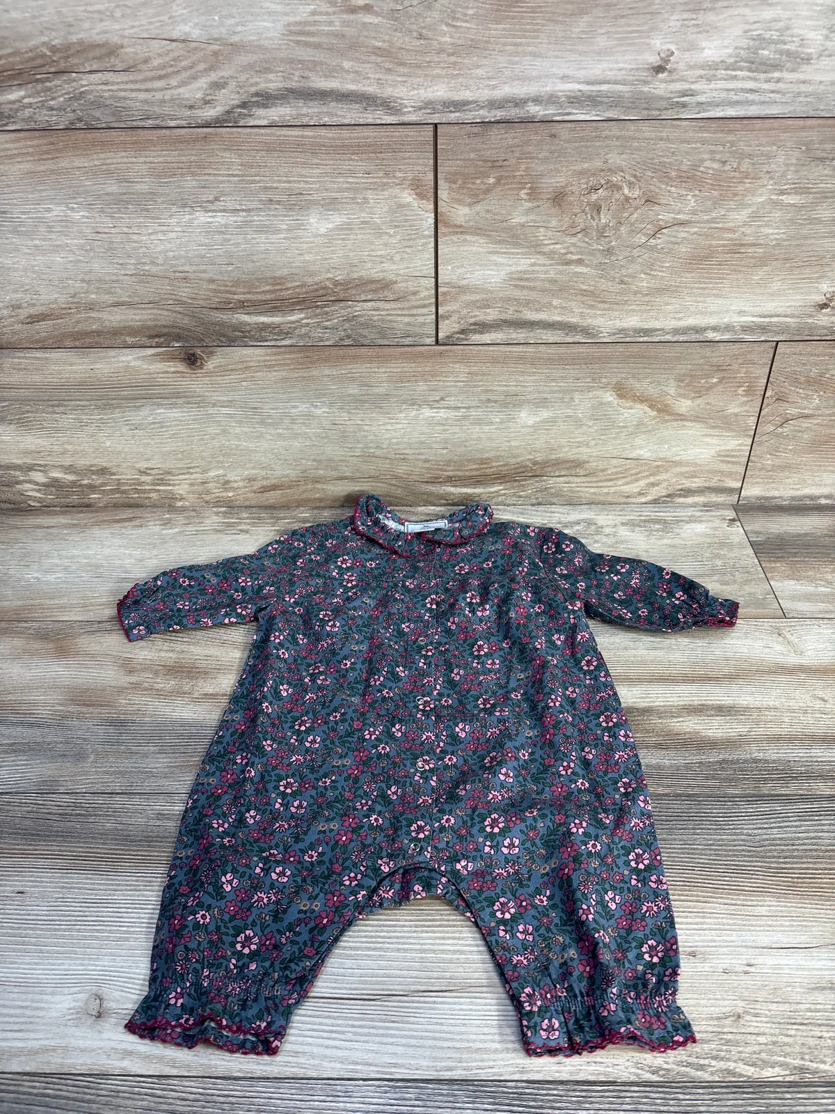 Front view of Petite Plume Twill Madeline romper in blue showcasing floral print, collar, and long sleeves on wood flooring