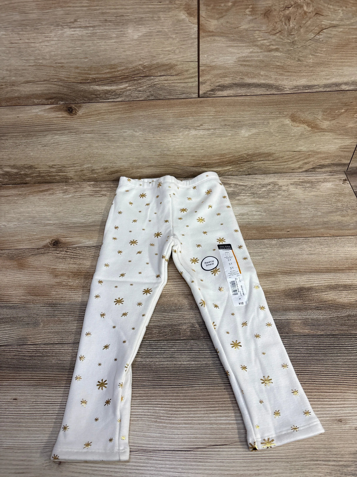 Toddler fleece-lined white leggings with gold star print on wooden floor