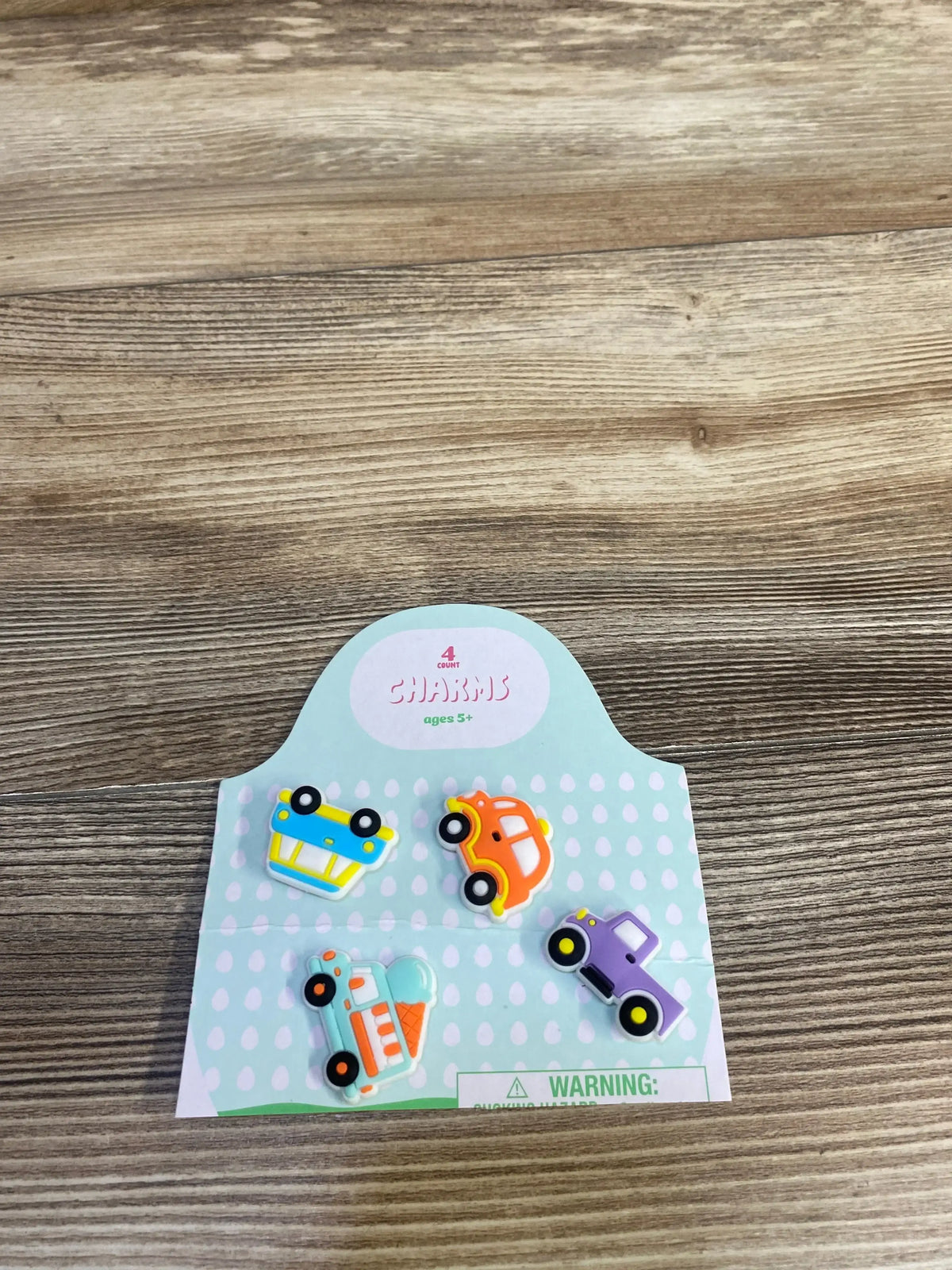 Top-down of 4-pack kids’ vehicle charms showcasing colorful car and truck shapes on a mint polka-dot display card on a wood table