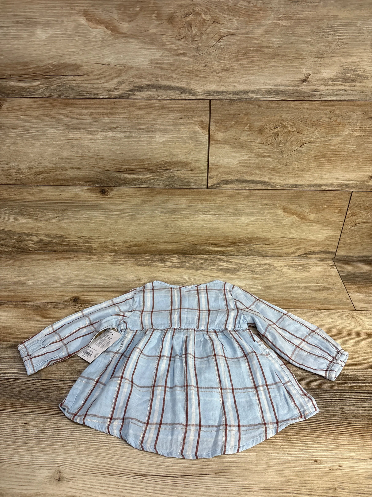 Light blue plaid long-sleeve baby dress with brown and white stripes on wooden surface