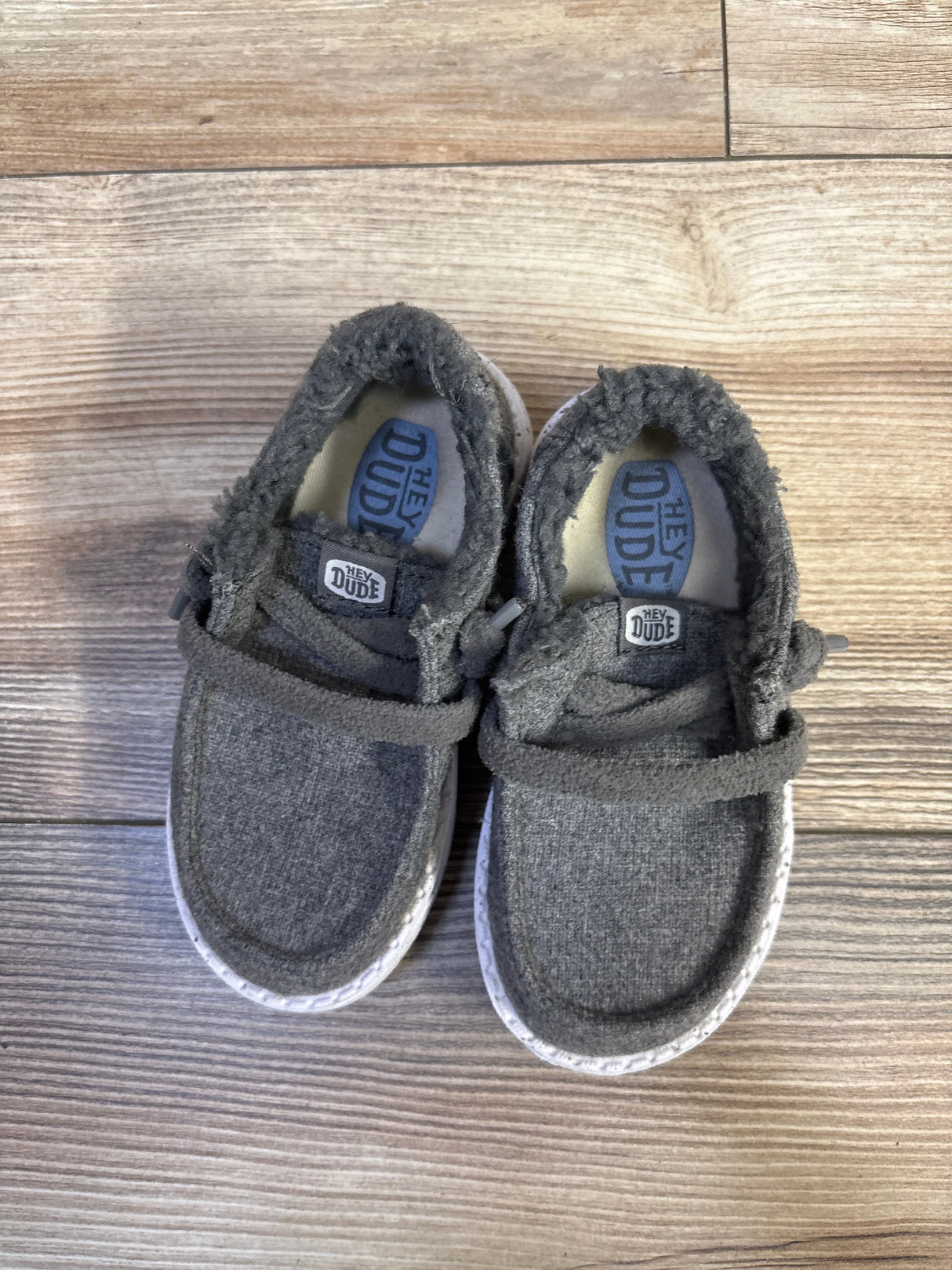 Top view of Hey Dude Wendy Wool cozy kids shoes size 7C showing grey wool upper, fuzzy collar, elastic laces on wood floor