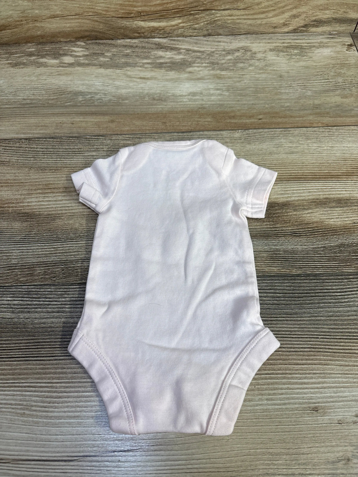 Back view of Primary ladybug bodysuit in pink showcasing short sleeves and leg openings on a wood-grain background