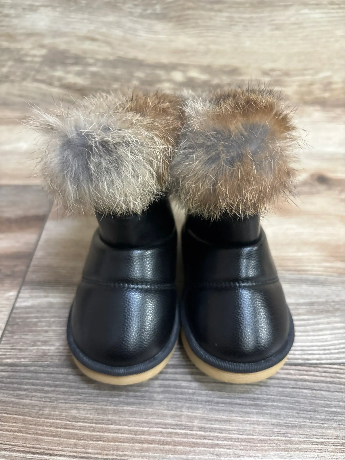 Children’s black winter boots with faux fur trim and tan rubber soles on wood floor