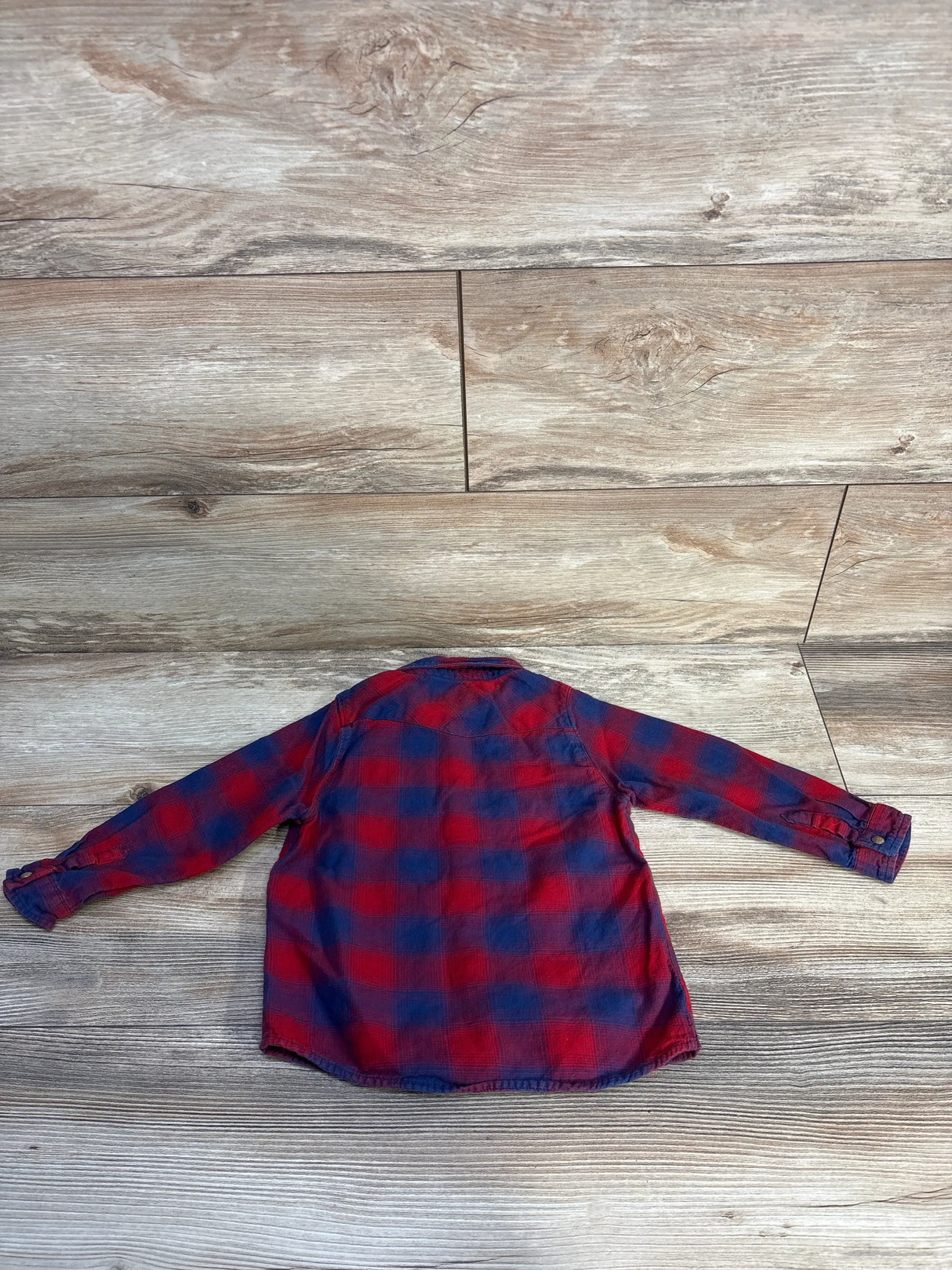 Red and navy plaid flannel shirt with long sleeves on wood background