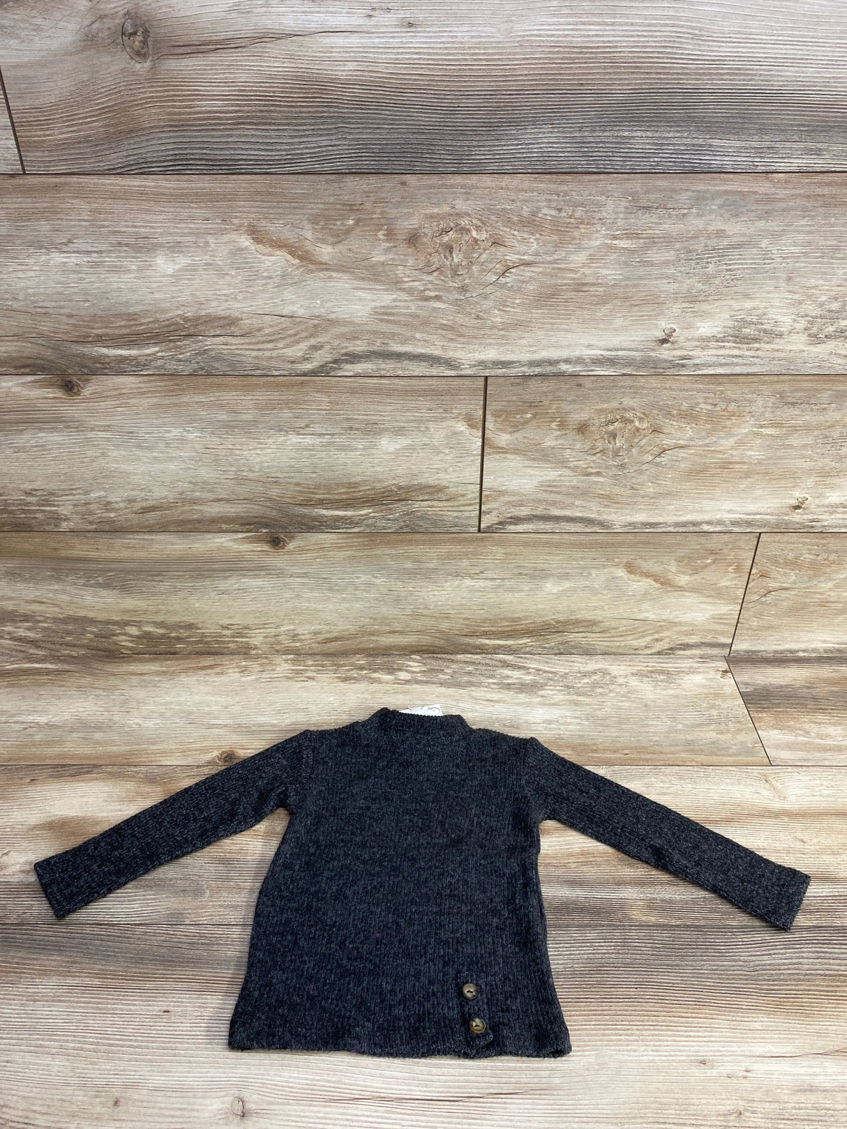 Dark gray long-sleeve knit toddler sweater with two brown buttons on wooden floor