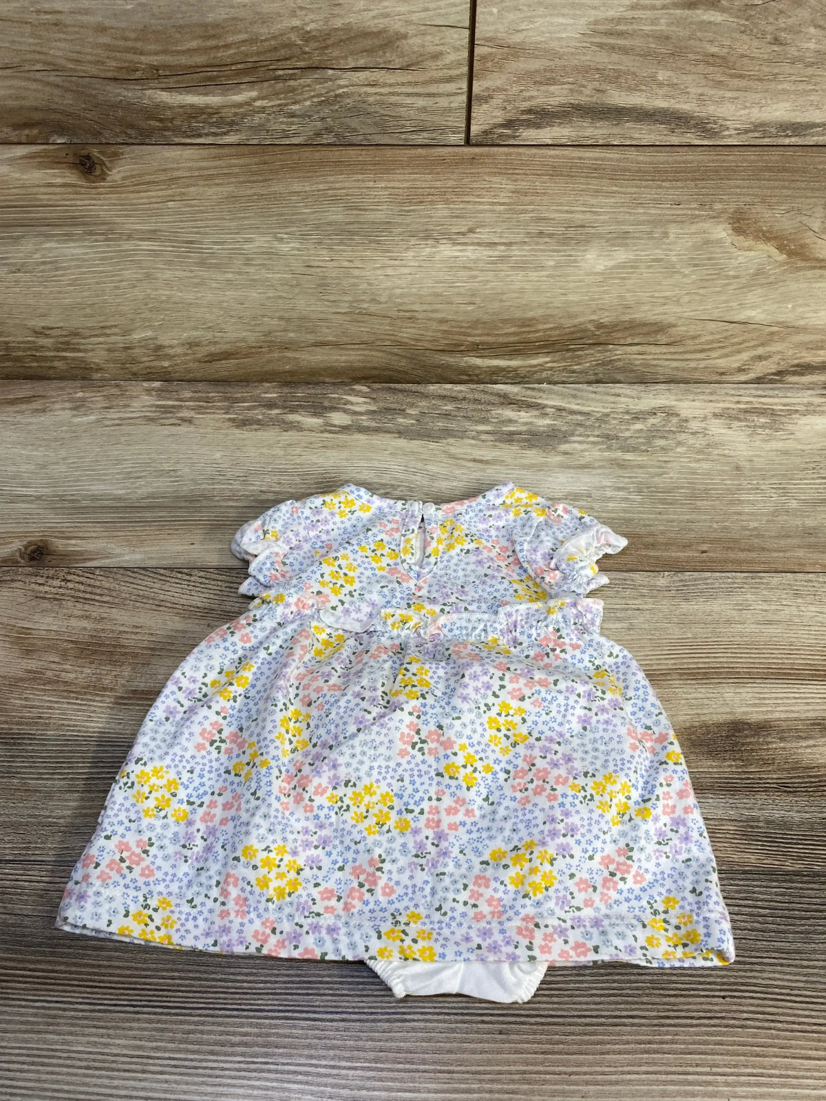 Front view of baby floral dress with matching bloomers, ruffle sleeves and yellow-pink-purple floral print on light wood floor