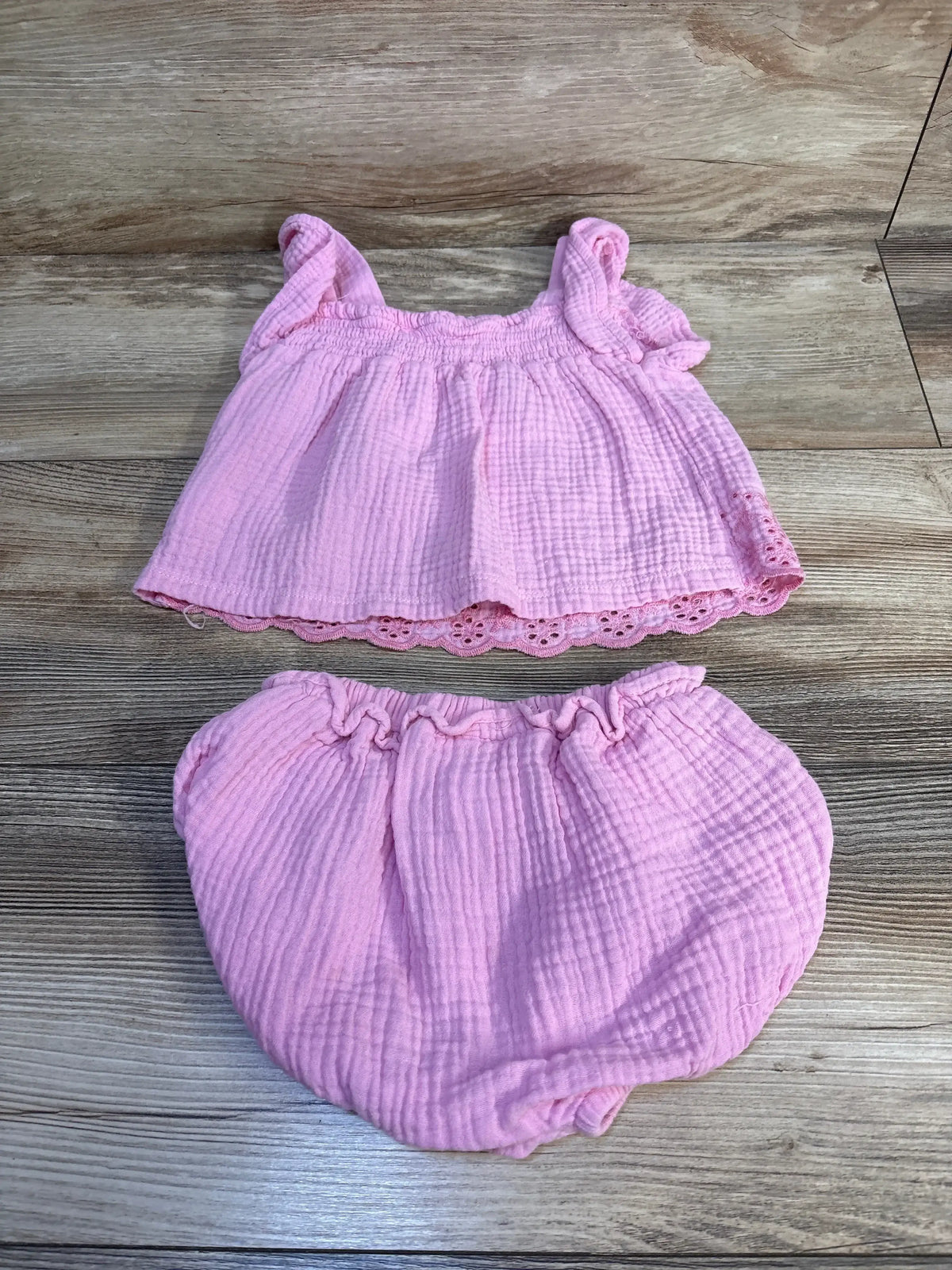Pink baby girl 2-piece outfit with ruffled top and bloomers, soft muslin fabric, layflat on wood floor