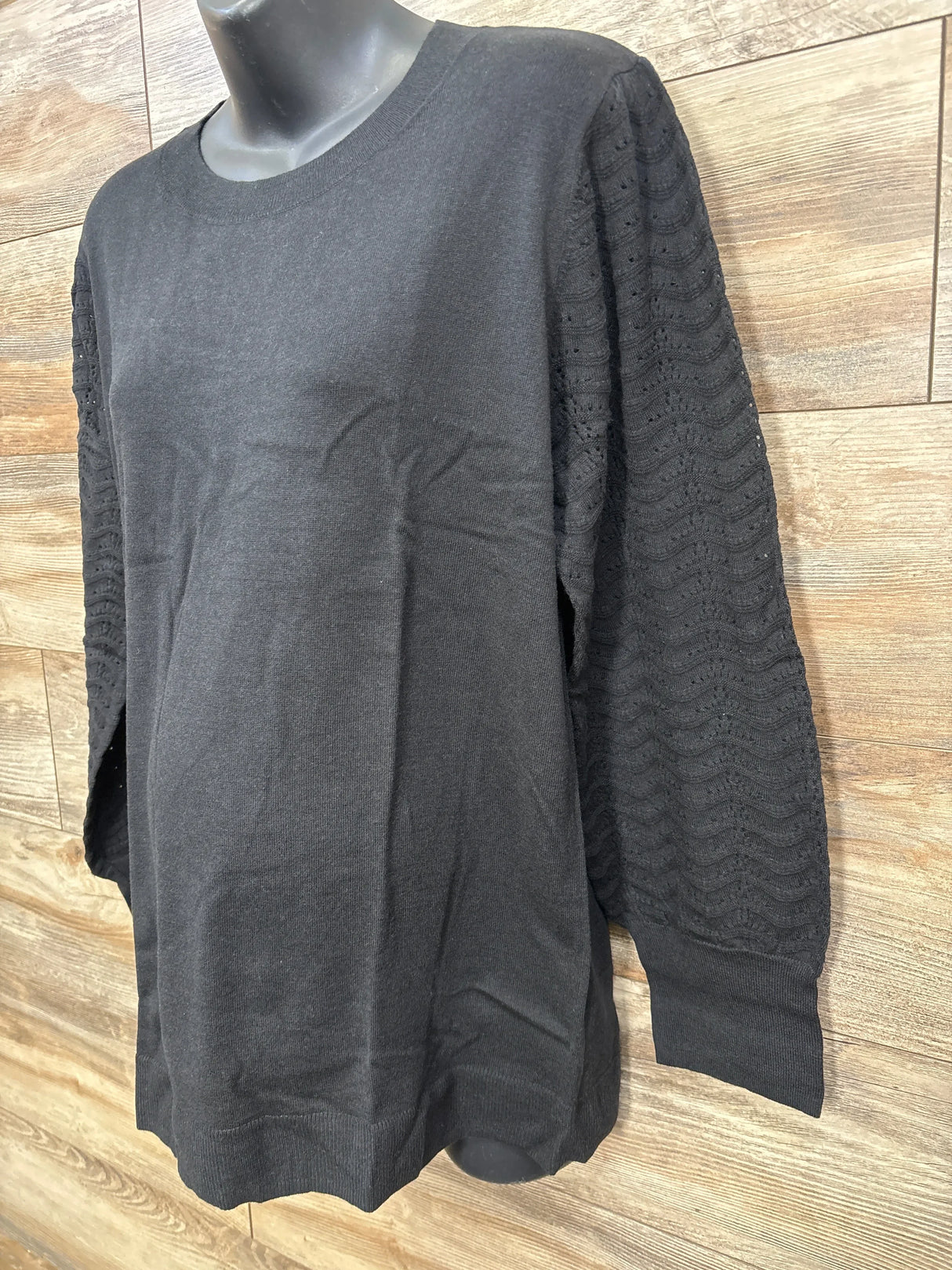 Black sweater with textured wave pattern sleeves on mannequin against wooden wall background