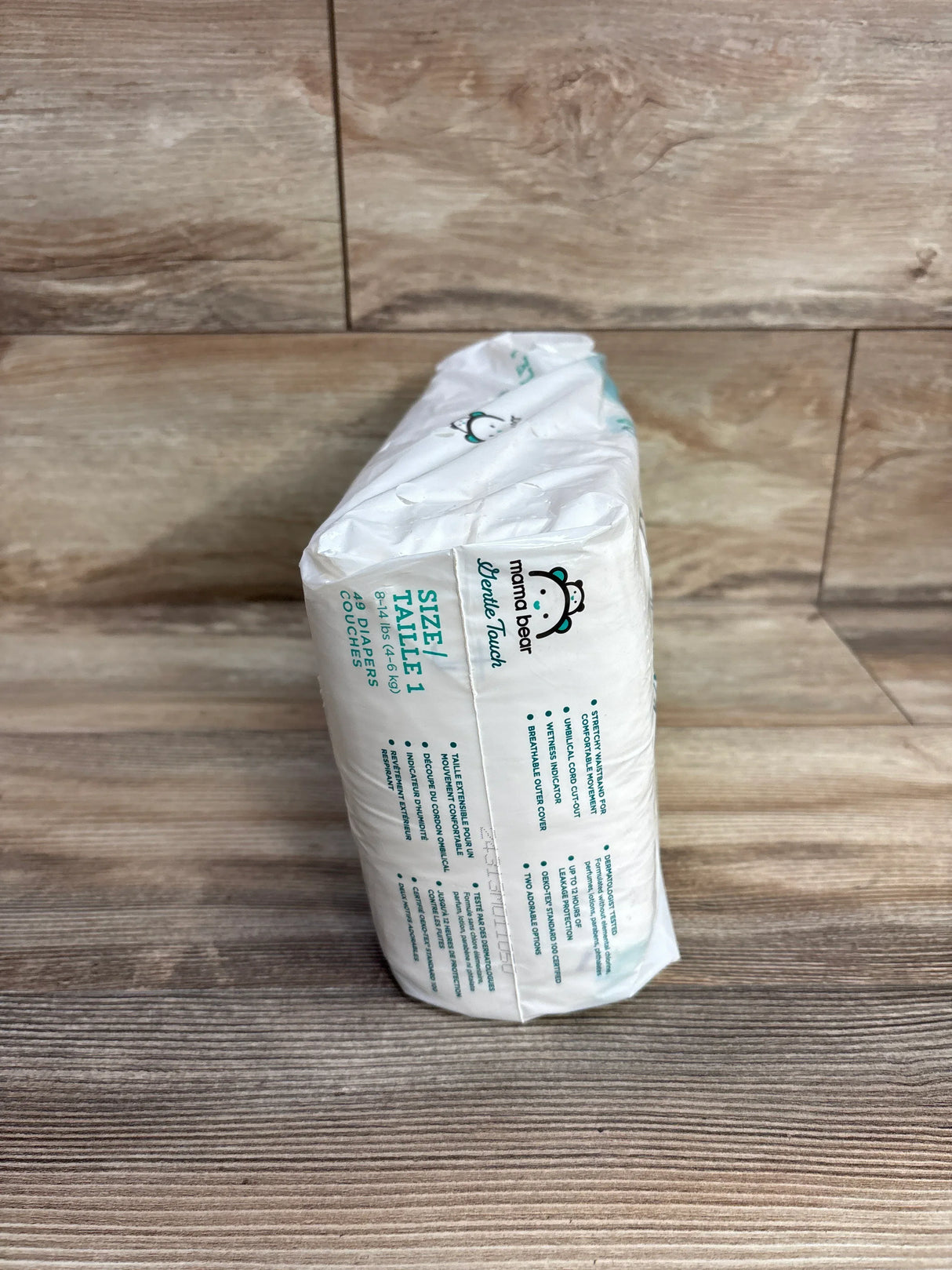 Angled view of Mama Bear Gentle Touch Size 1 diaper pack (8–14 lb, 49 count) showing size label and packaging text on wooden surface