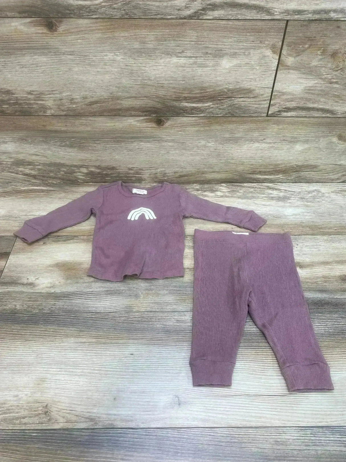 Flat lay of impidimpi ribbed baby shirt and matching pants in purple, size 3 months, white rainbow on wood background