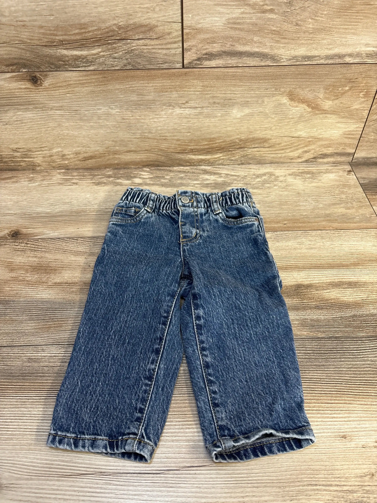 Front view of Cat and Jack paperbag pants, size 18M, showcasing dark wash denim and elastic waistband on wooden floor