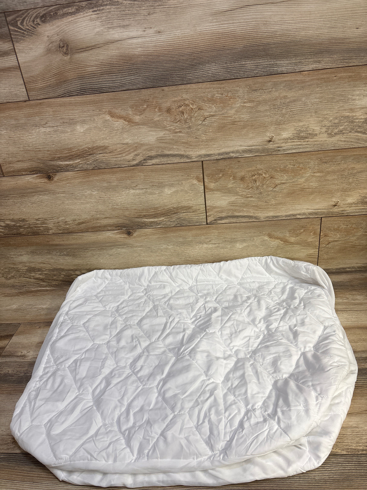 Top down view of Amfori waterproof crib mattress protector showing quilted top and elastic skirt on wood floor