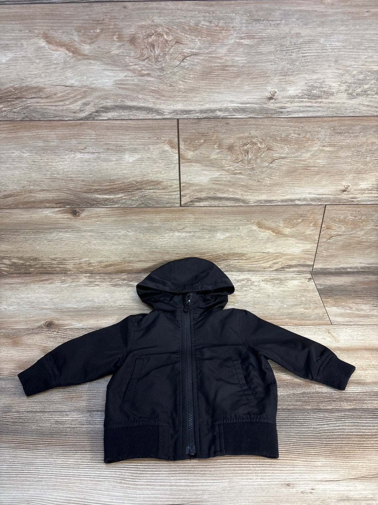 Black kids hooded jacket with zipper, laid flat on wood floor for resale
