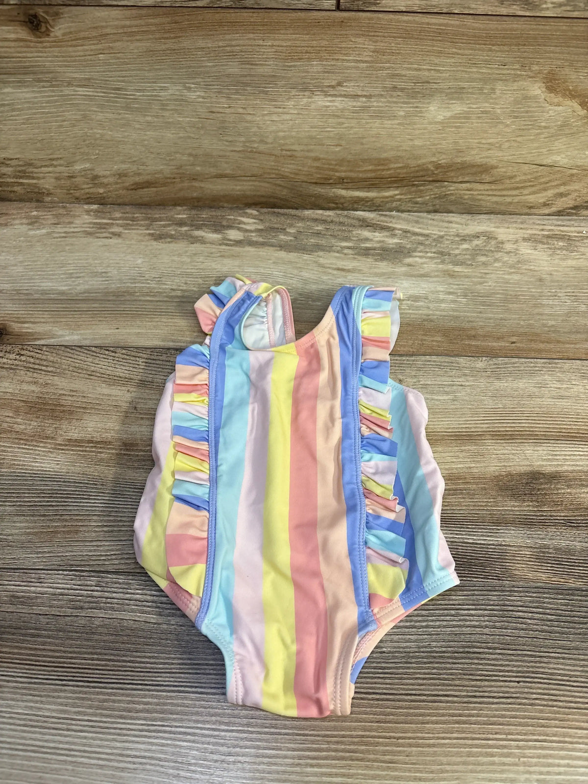 Front view of Starting Out 1pc striped swimsuit showcasing pastel vertical stripes and ruffle sleeves on a wood-grain background