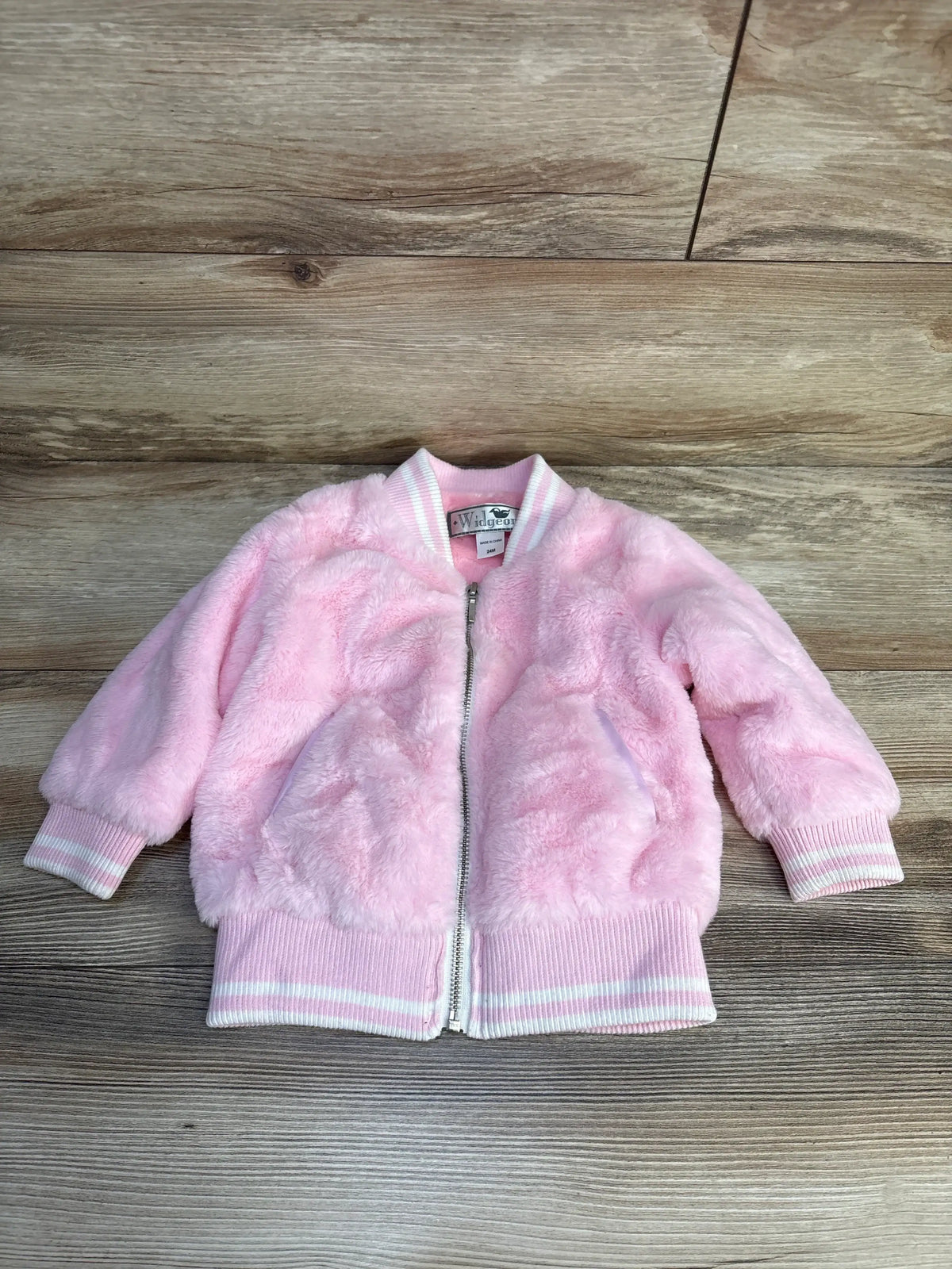 Pink fuzzy baby bomber jacket with white stripes, size 24M, laid on wood floor